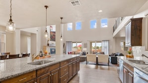 A spacious kitchen with a large island, wooden cabinets, and pendant lighting. There is a dining area with chairs and a sofa. - Paintbrush Retreat #65 by RedAwning (Ivins)