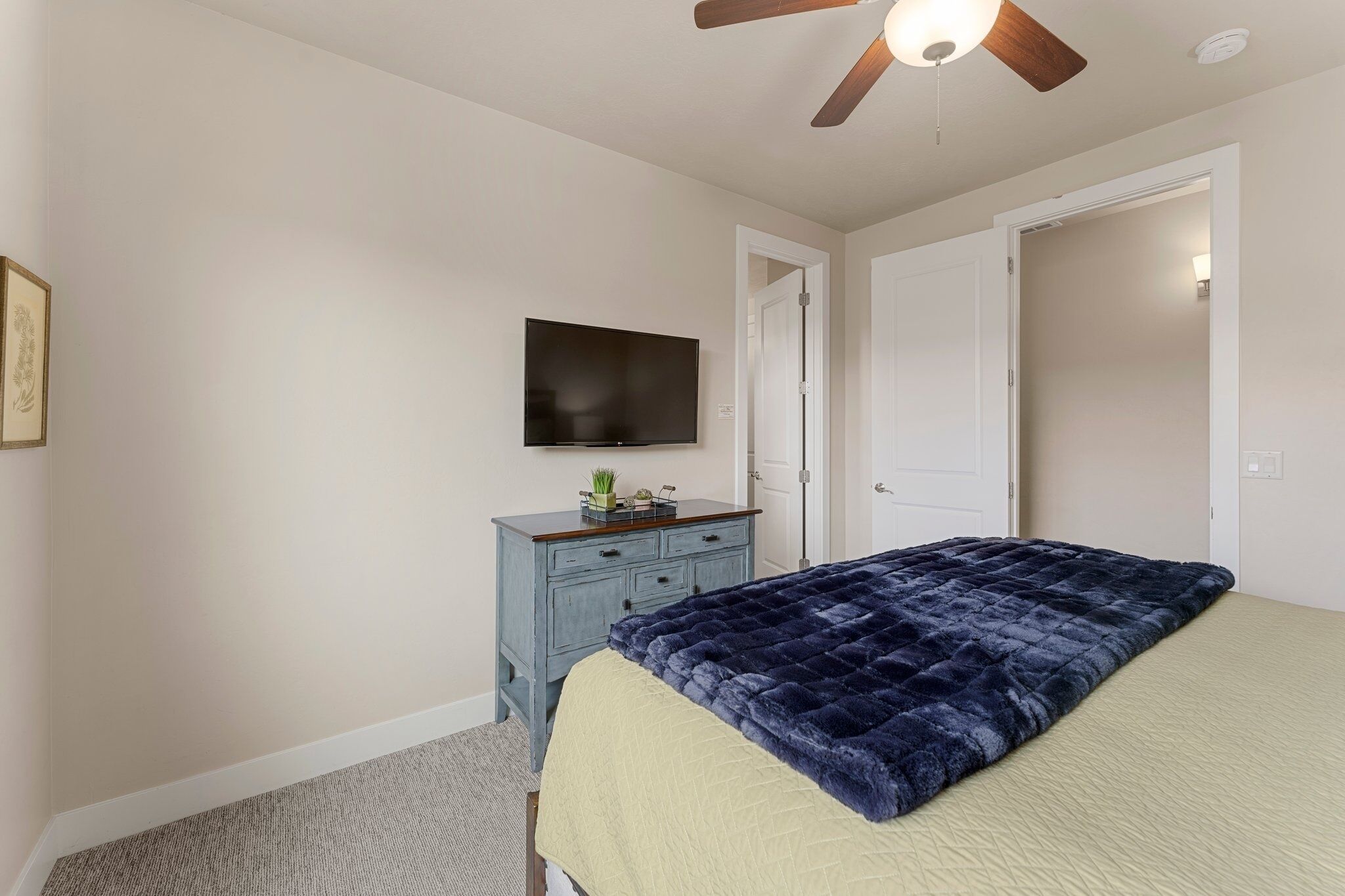 A bedroom with a bed, a dresser, a television, and a ceiling fan.