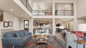 A spacious living area with a high ceiling, a kitchen in the background, and a balcony with a railing. - Paintbrush Retreat #65 by RedAwning (Ivins)