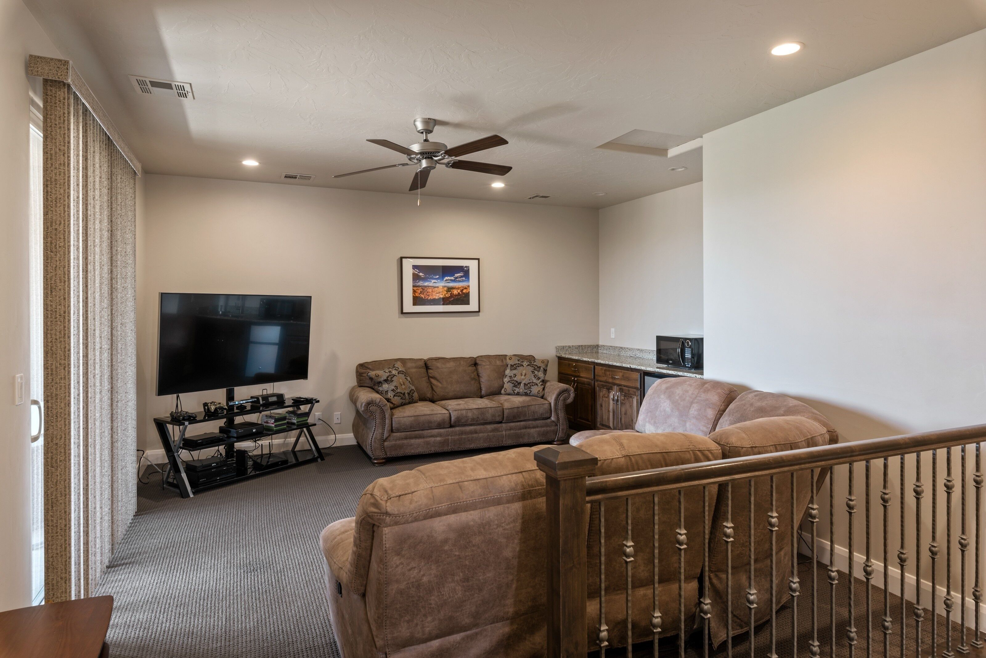 A living room with a flat-screen TV, a ceiling fan, a sofa, a coffee table, and a staircase railing.