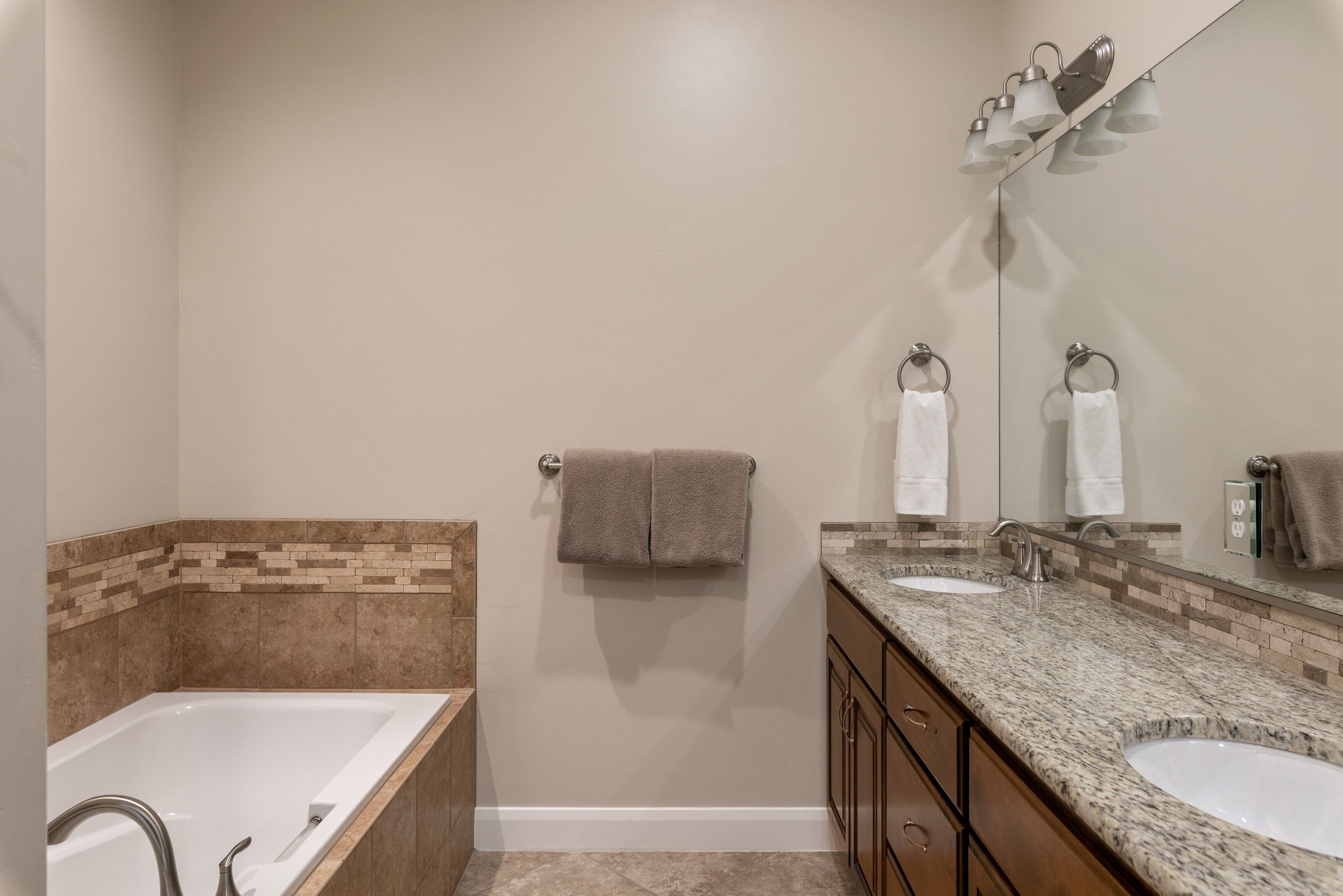A bathroom with a bathtub, two sinks, a vanity with a mirror, and a towel rack.