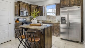 A modern kitchen with wooden cabinets, stainless steel appliances, a granite countertop, and a bar area with stools. - Mountain View by RedAwning (Washington)