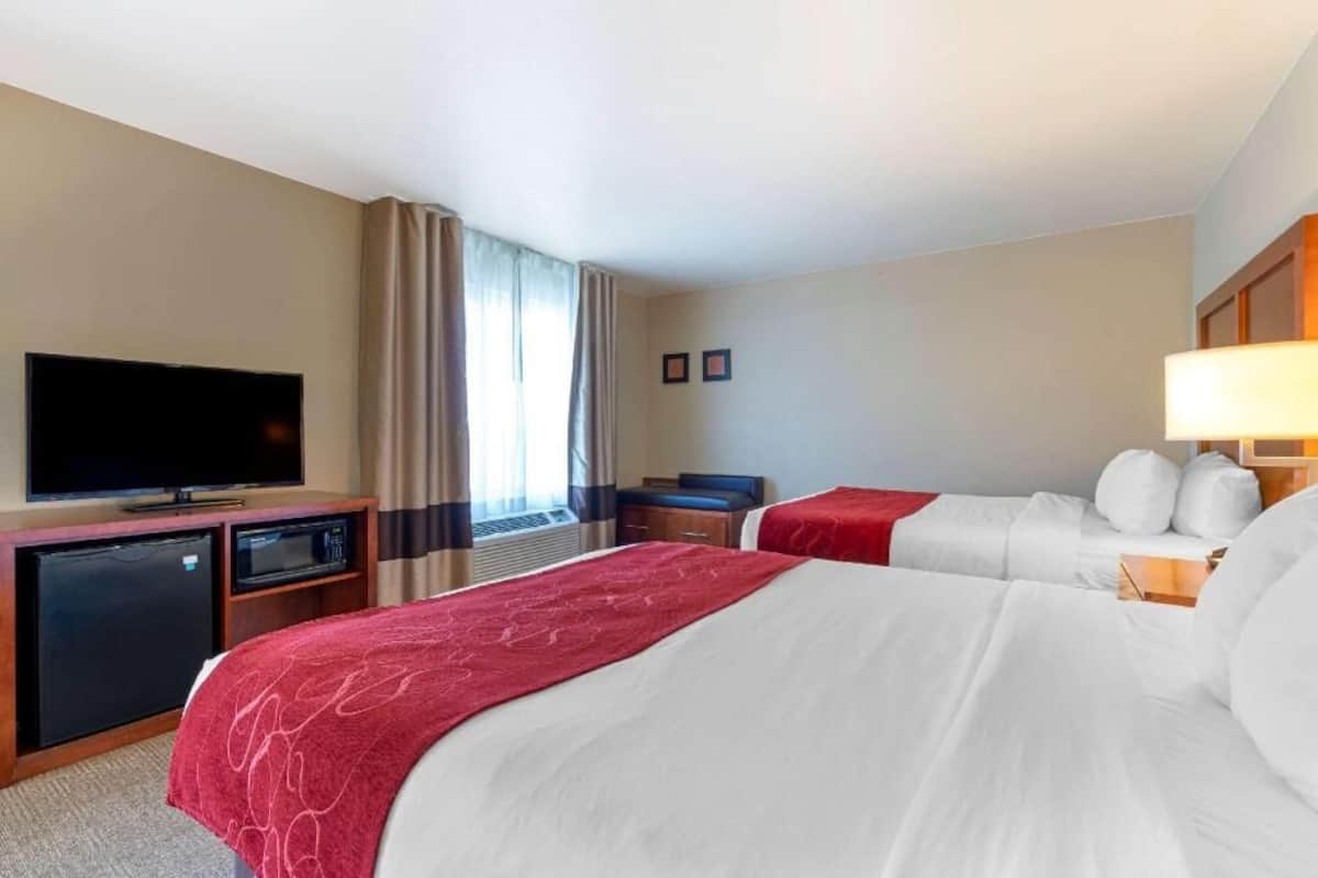 A hotel room with two beds, a TV, a mini-fridge, a microwave, and a desk.