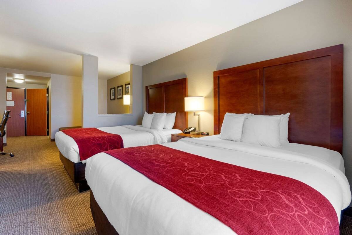 A hotel room with two beds, a desk, a chair, a lamp, and a door.