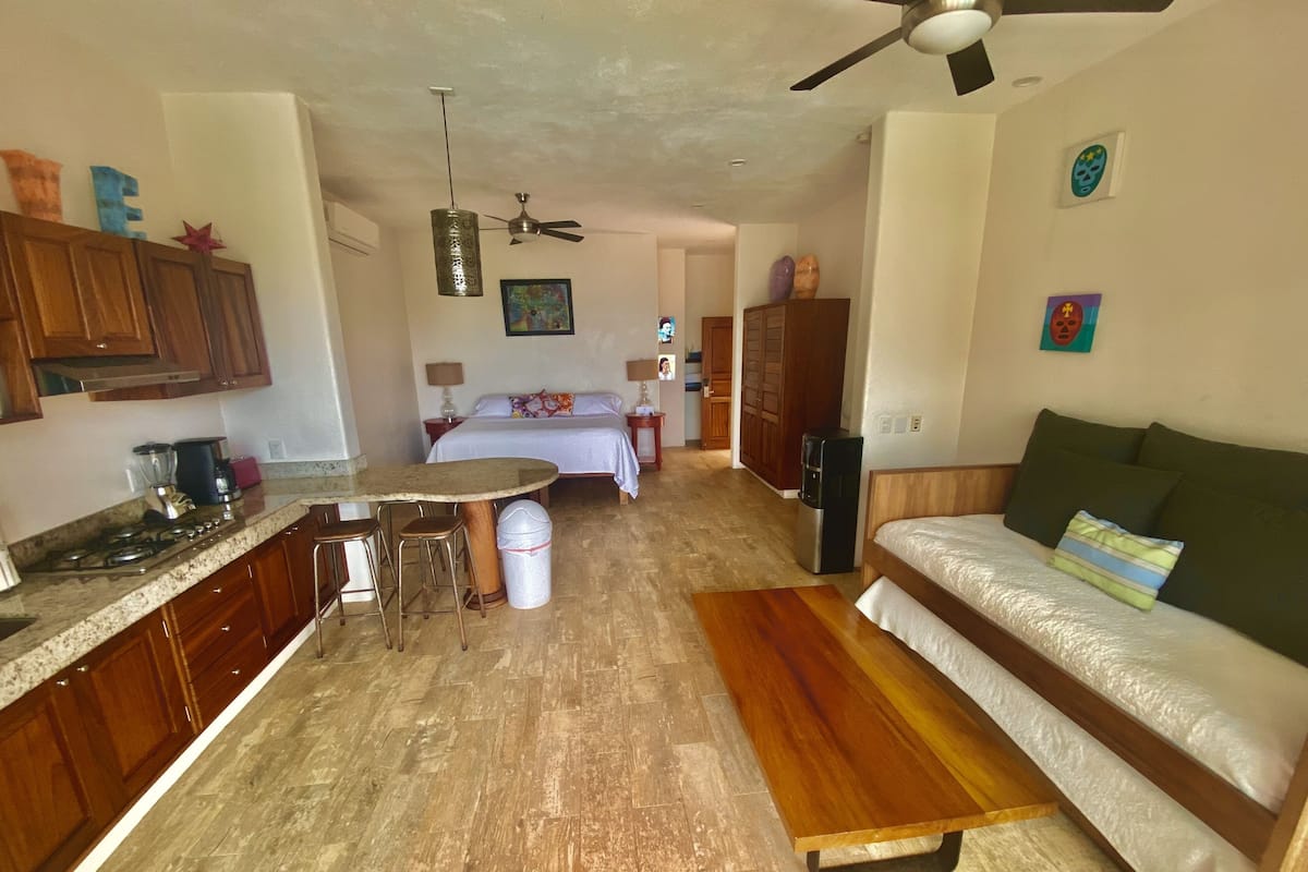 A compact living space with a kitchenette, a bed, a sofa, and a ceiling fan.