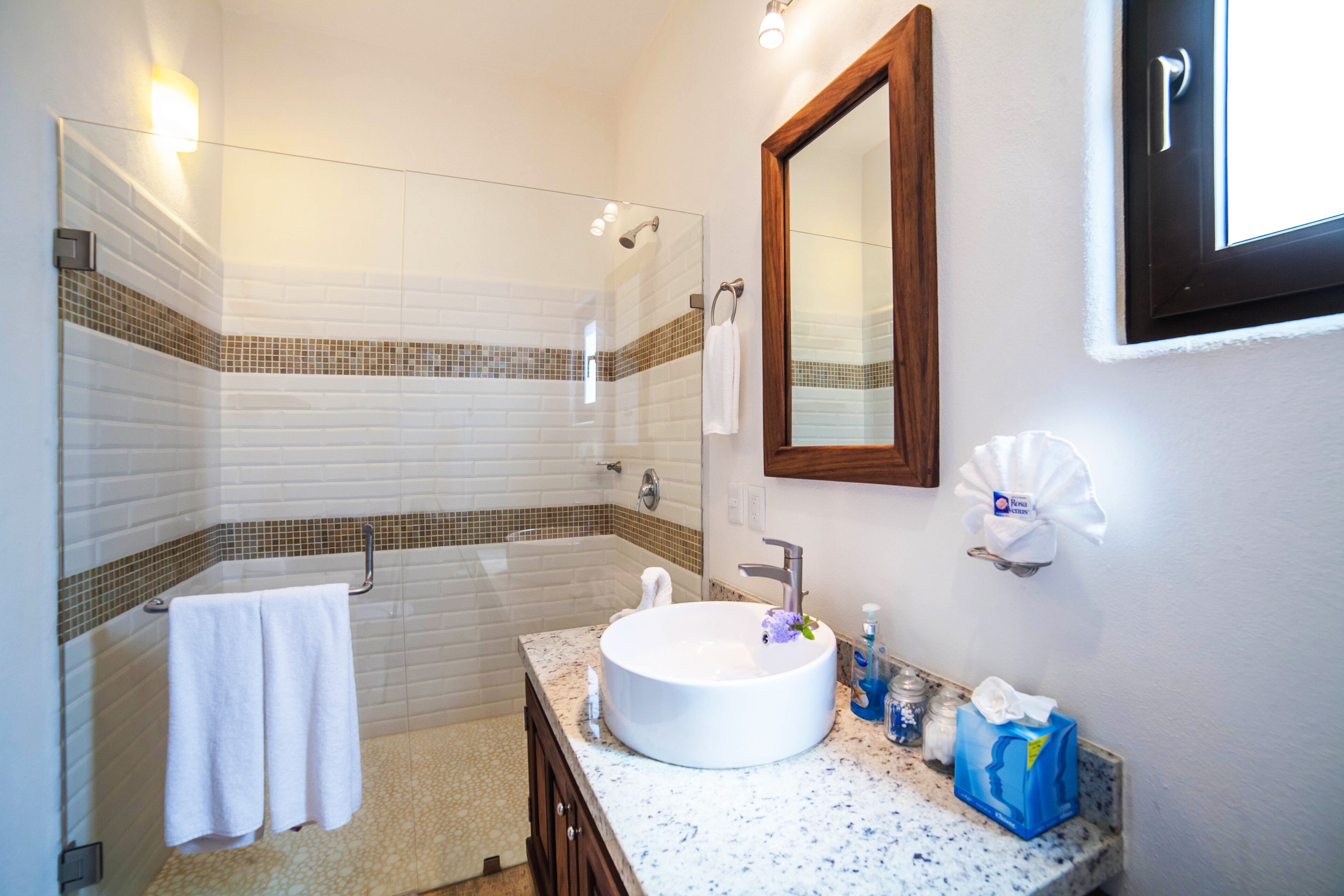A modern bathroom with a glass-enclosed shower, a white sink, and a wooden-framed mirror.