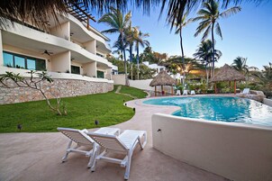 Um resort com piscina, cadeiras de sol brancas, palmeiras e um muro de pedra.