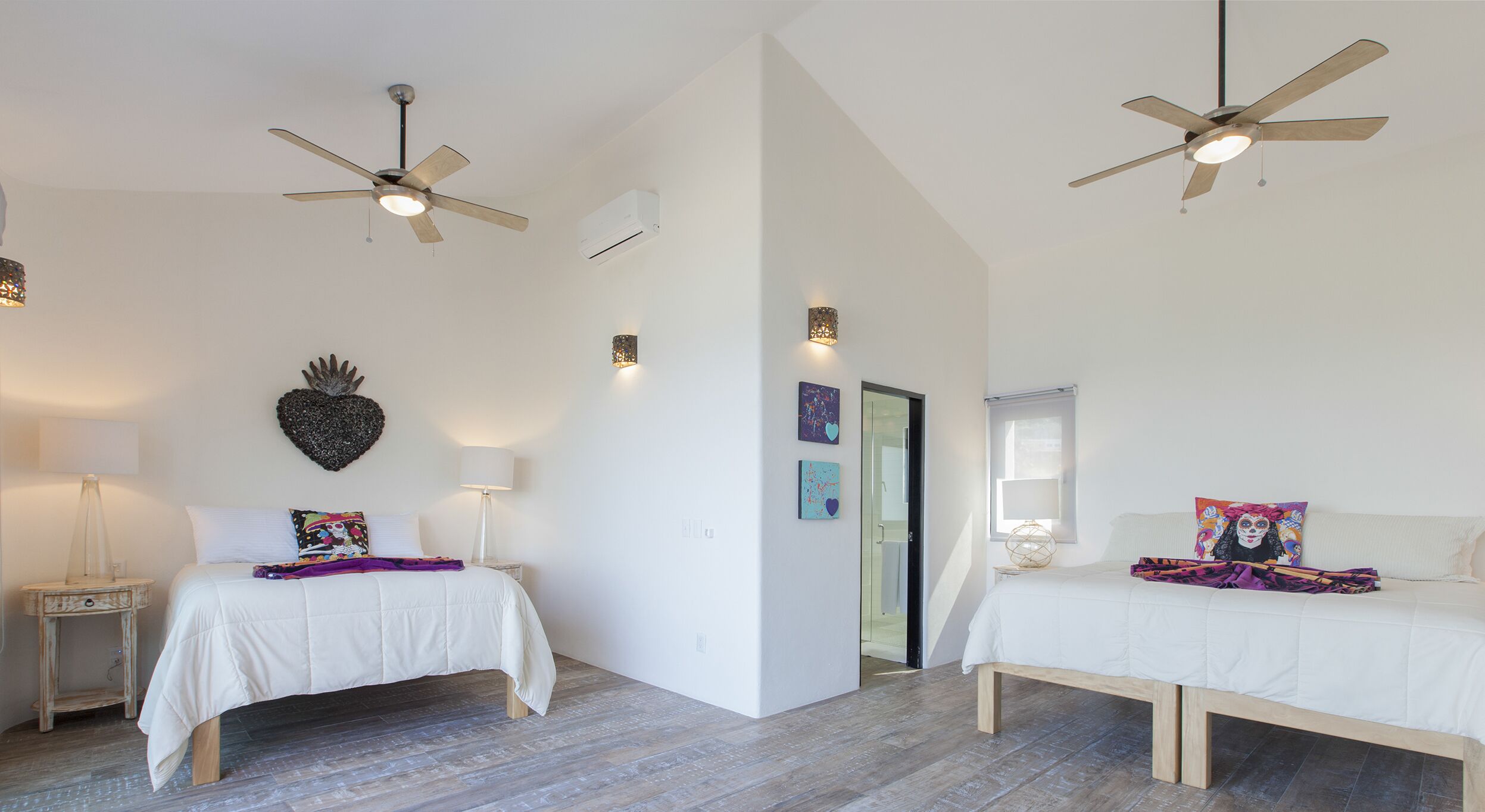 Une chambre moderne avec deux lits, des ventilateurs de plafond et un cœur décoratif accroché au mur.