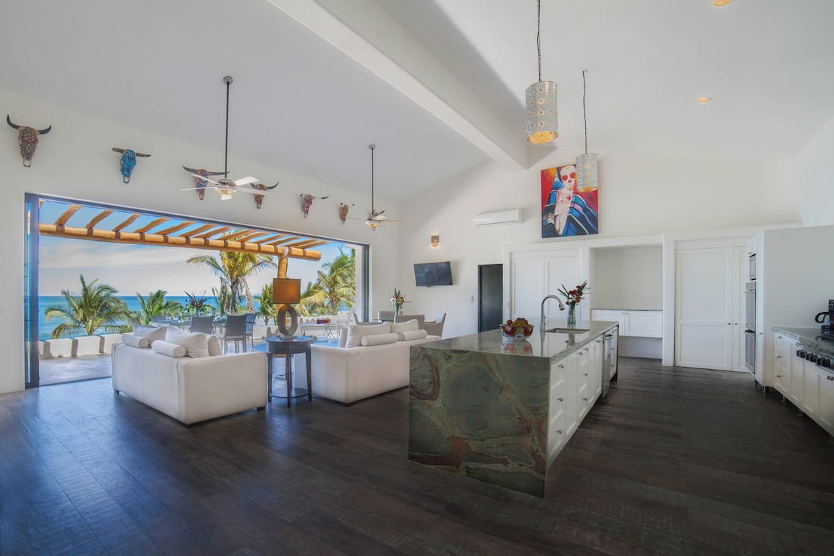 A spacious living area with a large island, a view of the ocean, and a modern kitchen with white cabinetry.