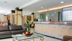 A hotel lobby with a reception desk, a sofa, a coffee table with a bowl and plant, and a patterned wall. - Palacio do Rio Hotel (Teresina)