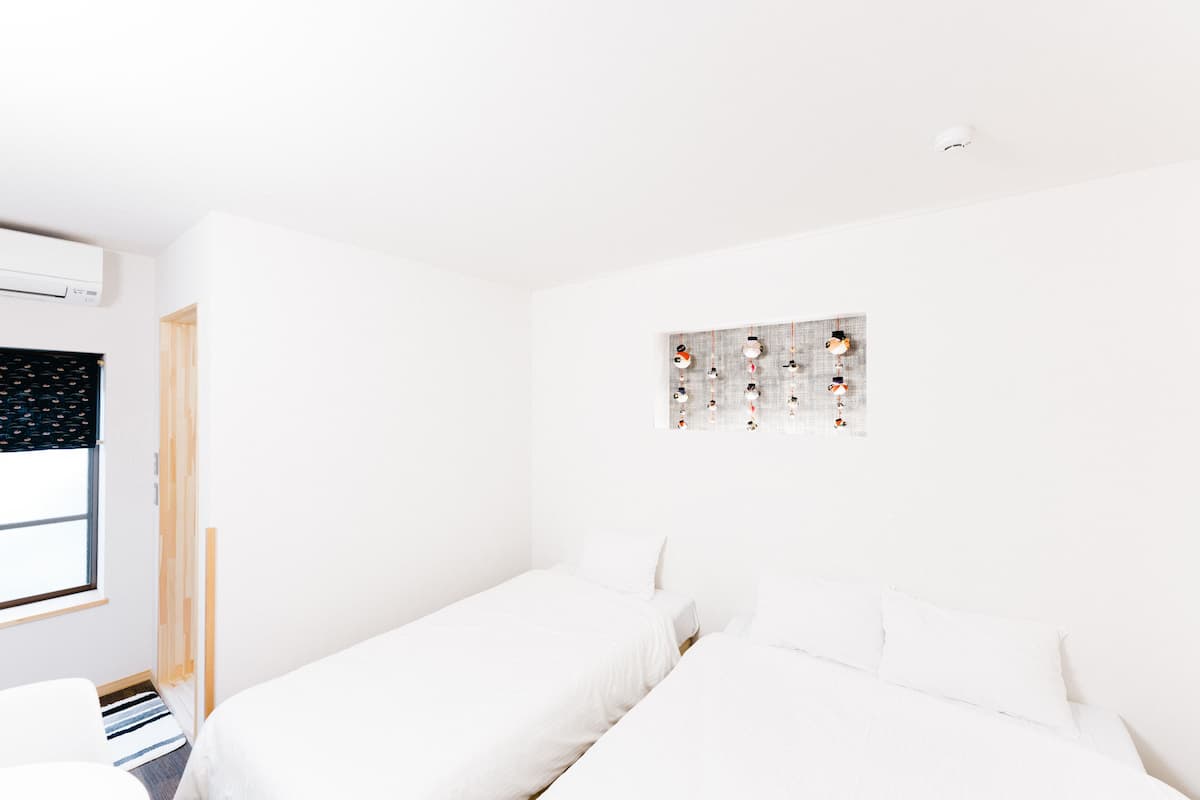 A minimalist room with two beds, a window with blinds, and a wall-mounted artwork.