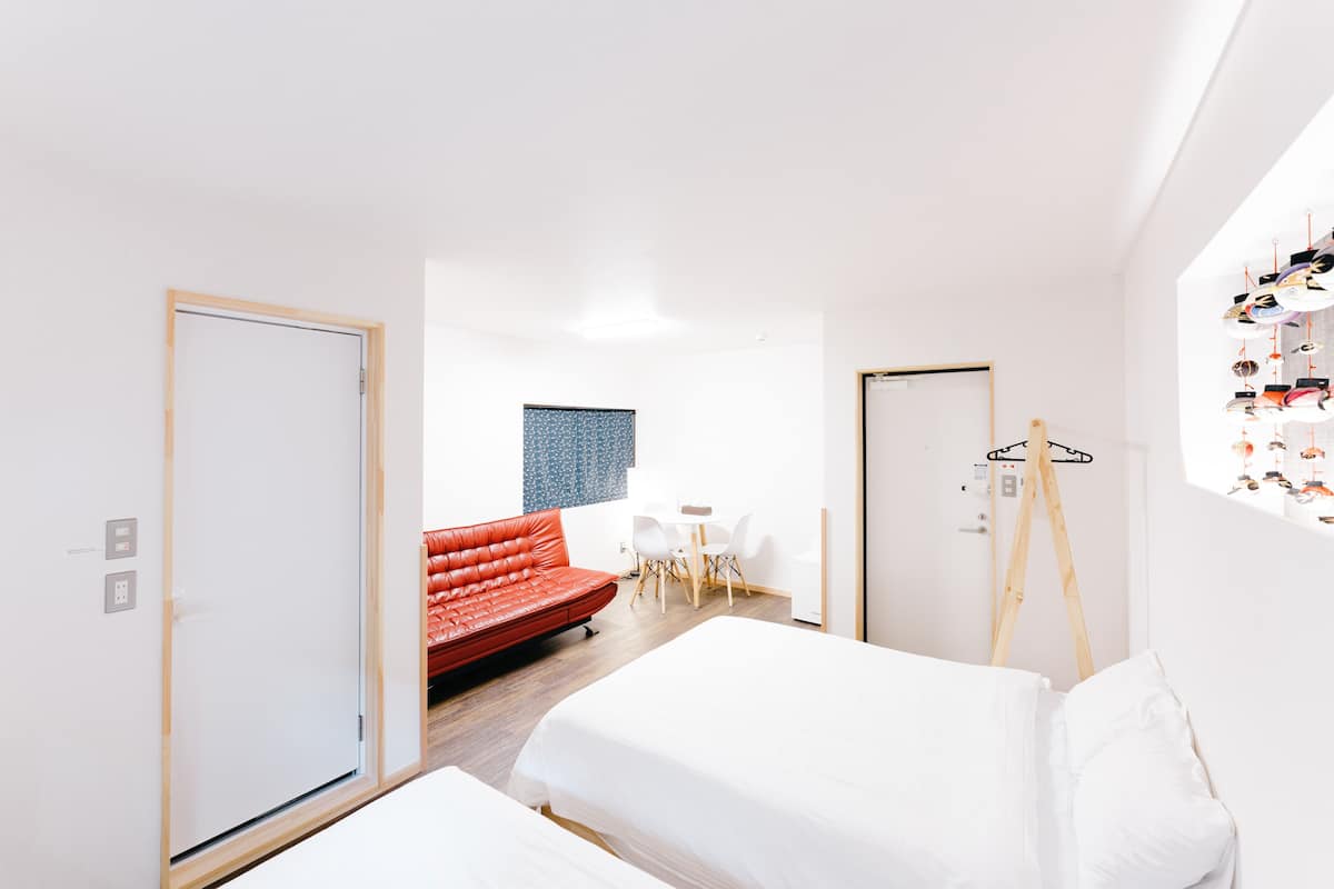 A modern hotel room with a bed, a red sofa, a small table, and a wardrobe.