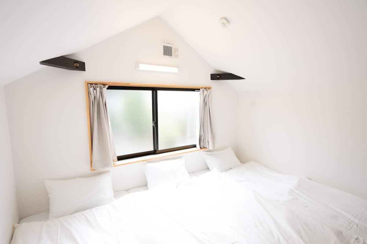 A bedroom with a large bed, a window with curtains, and a sloped ceiling with built-in lighting.
