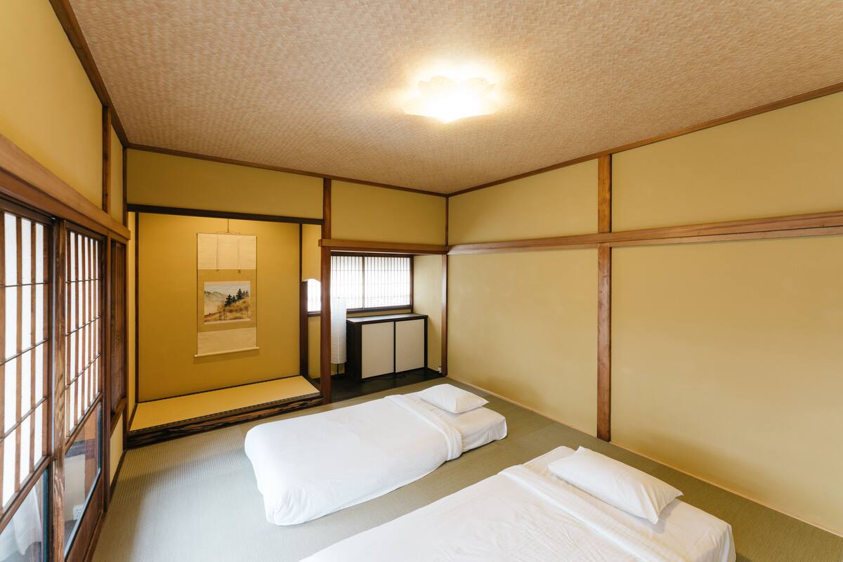 A traditional Japanese-style room with tatami flooring, two single beds, a shoji screen, and a small washbasin.