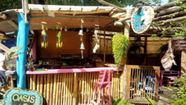 A rustic outdoor seating area with a bamboo fence, a wooden table, and a sign that reads "OASIS". - Oasis Hostal Restaurante (Maicao)