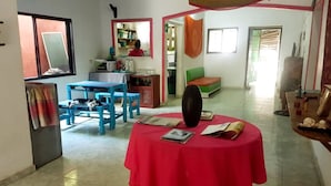A dining area with a red table, blue chairs, and a kitchen in the background. - Oasis Hostal Restaurante (Maicao)
