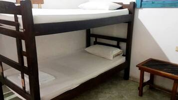 Una cama individual con estructura de madera, un colchón y una almohada. Junto a la cama hay una pequeña mesa de madera.