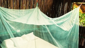 A bed with a mosquito net in a room with bamboo walls. - Oasis Hostal Restaurante (Maicao)