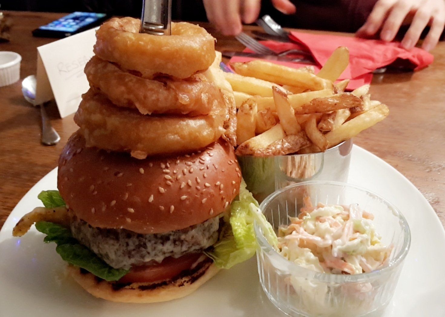A burger with onion rings, fries, and coleslaw on a plate.