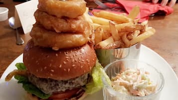 A burger with onion rings, fries, and coleslaw on a plate.