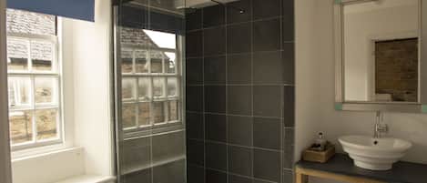 A bathroom with a shower, a sink, and a window.