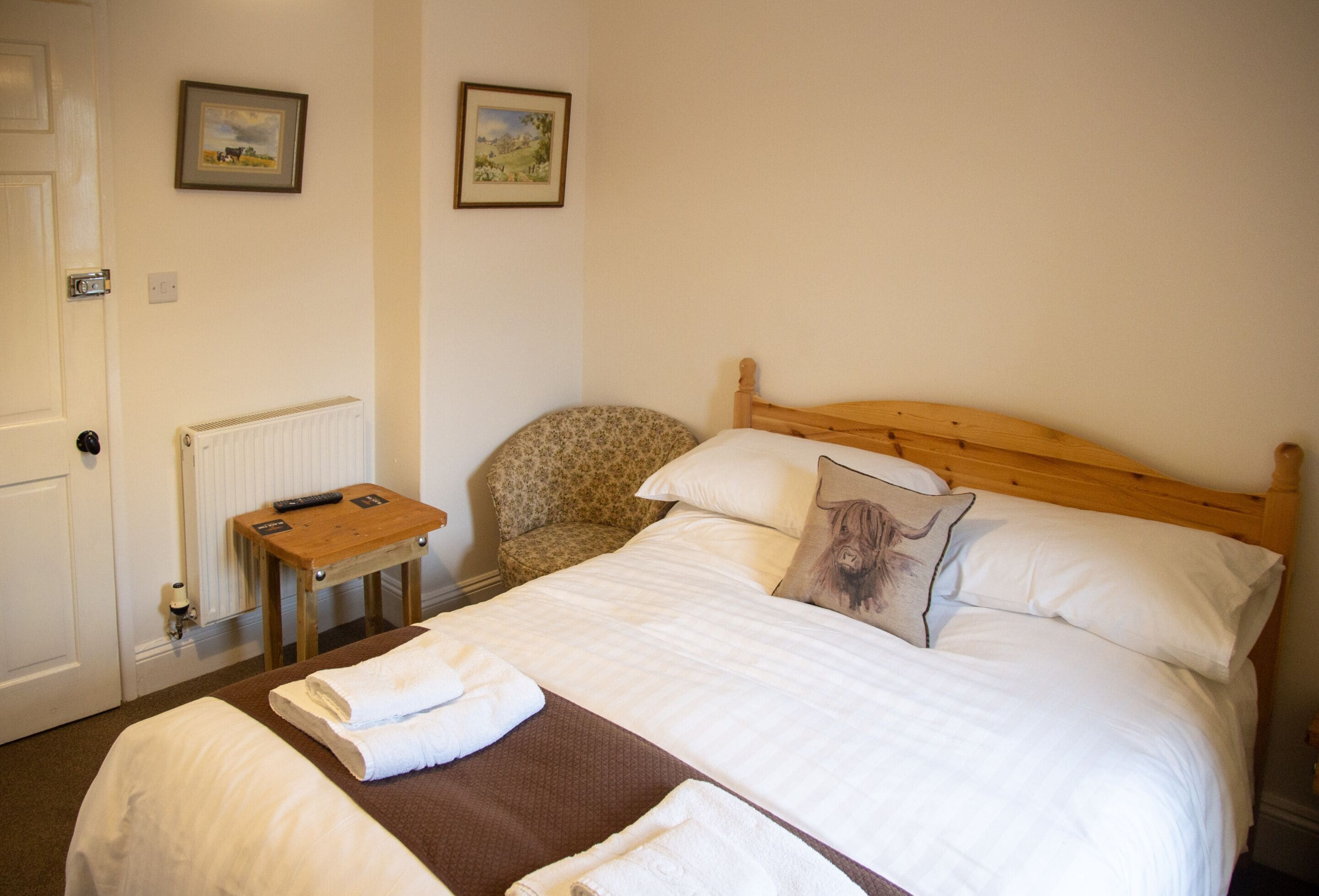 Ein Hotelzimmer mit Bett, Sessel, kleinem Tisch und zwei gerahmten Bildern an der Wand.