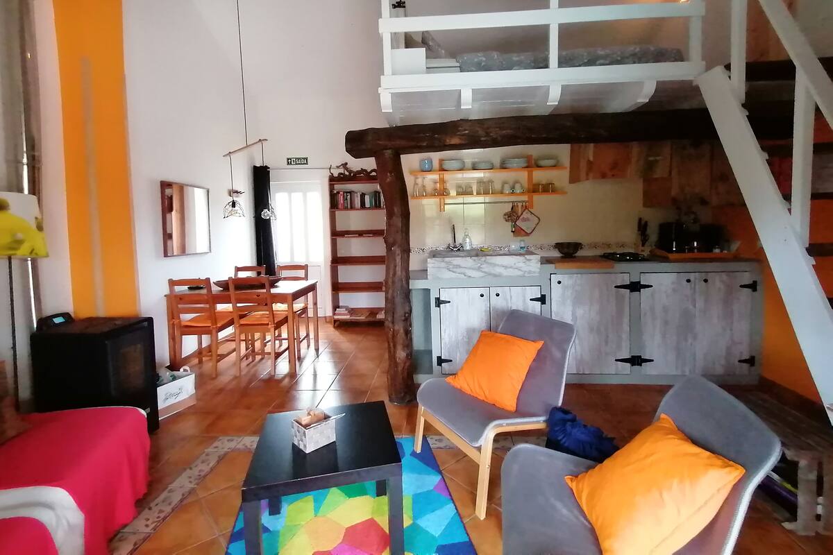 A cozy living room with a dining area, a staircase leading to an upper level, and a kitchen with wooden cabinets and shelves.