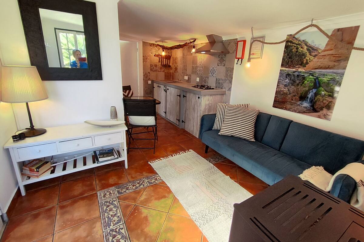 A living room with a sofa, a coffee table, a lamp, a TV, a bookshelf, and a kitchen area with cabinets and a stove.