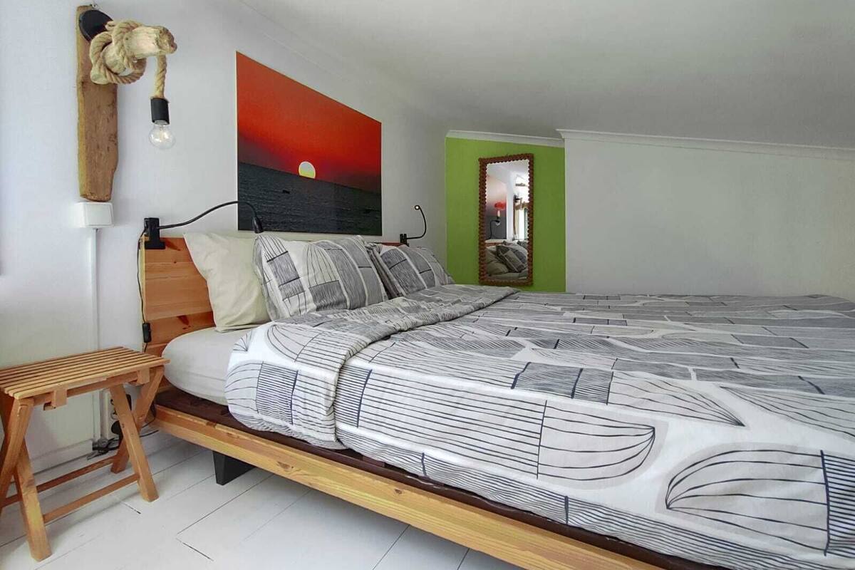 A bedroom with a bed, a wooden headboard, a nightstand, a lamp, a painting, and a mirror.