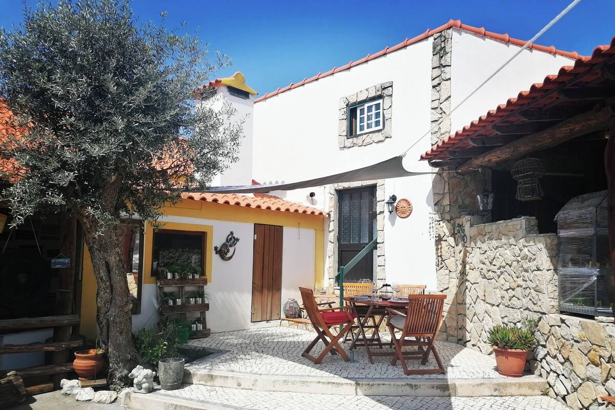 A building with a stone facade, a tiled roof, and a patio with a table and chairs.