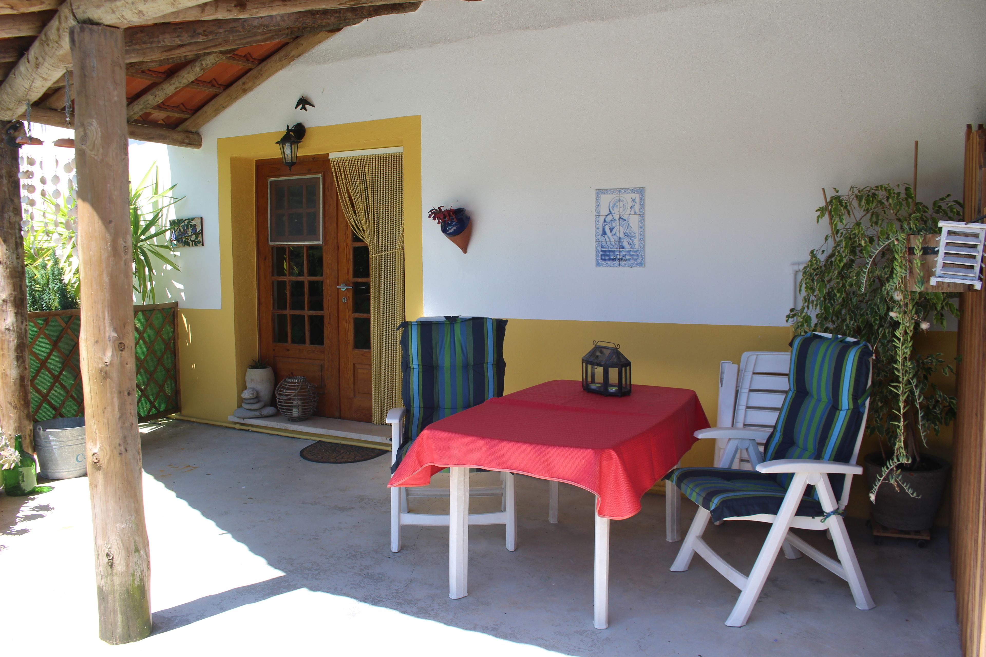 A covered patio with a table and two chairs, a wooden door, and a potted plant.