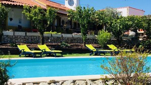 Une piscine avec des chaises longues, un mur en pierre et un bâtiment doté d’un toit en tuiles et d’un clocher.