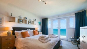 Habitació d'hotel amb un llit, una taula de nit, un armari i vista a l'oceà a través d'una porta corredissa de vidre.