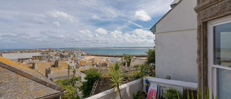 A balcony with a view of the sea and town, stone walls, and potted plants.