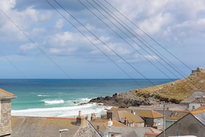 A coastal town with buildings near the sea, power lines, and rocky terrain. - Hepworth Apartment (St Ives)