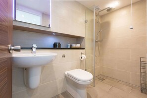 A modern bathroom with a sink, toilet, and glass-enclosed shower. - Hepworth Apartment (St Ives)