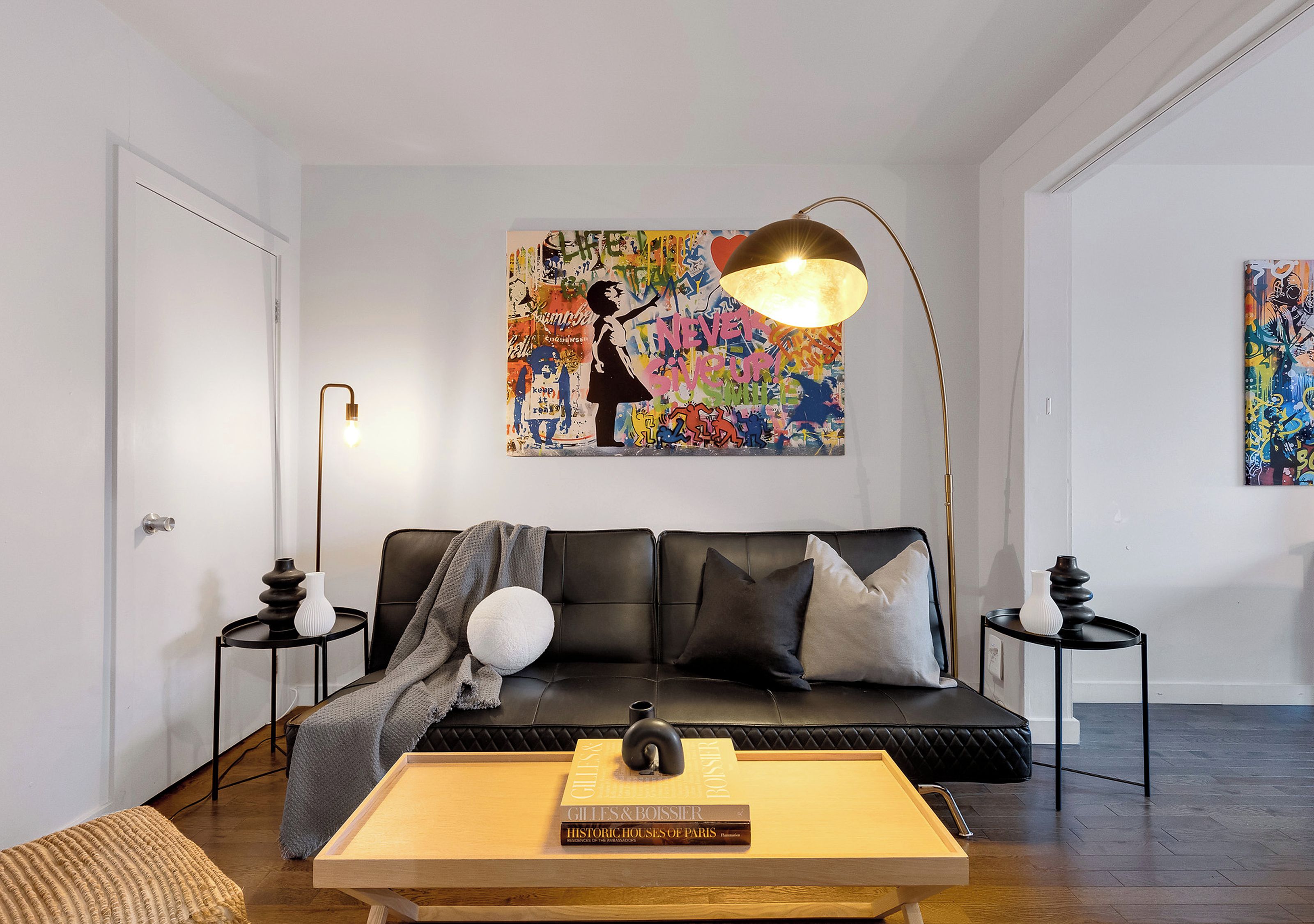 A modern living room with a black leather sofa, a wooden coffee table, and two side tables with lamps.