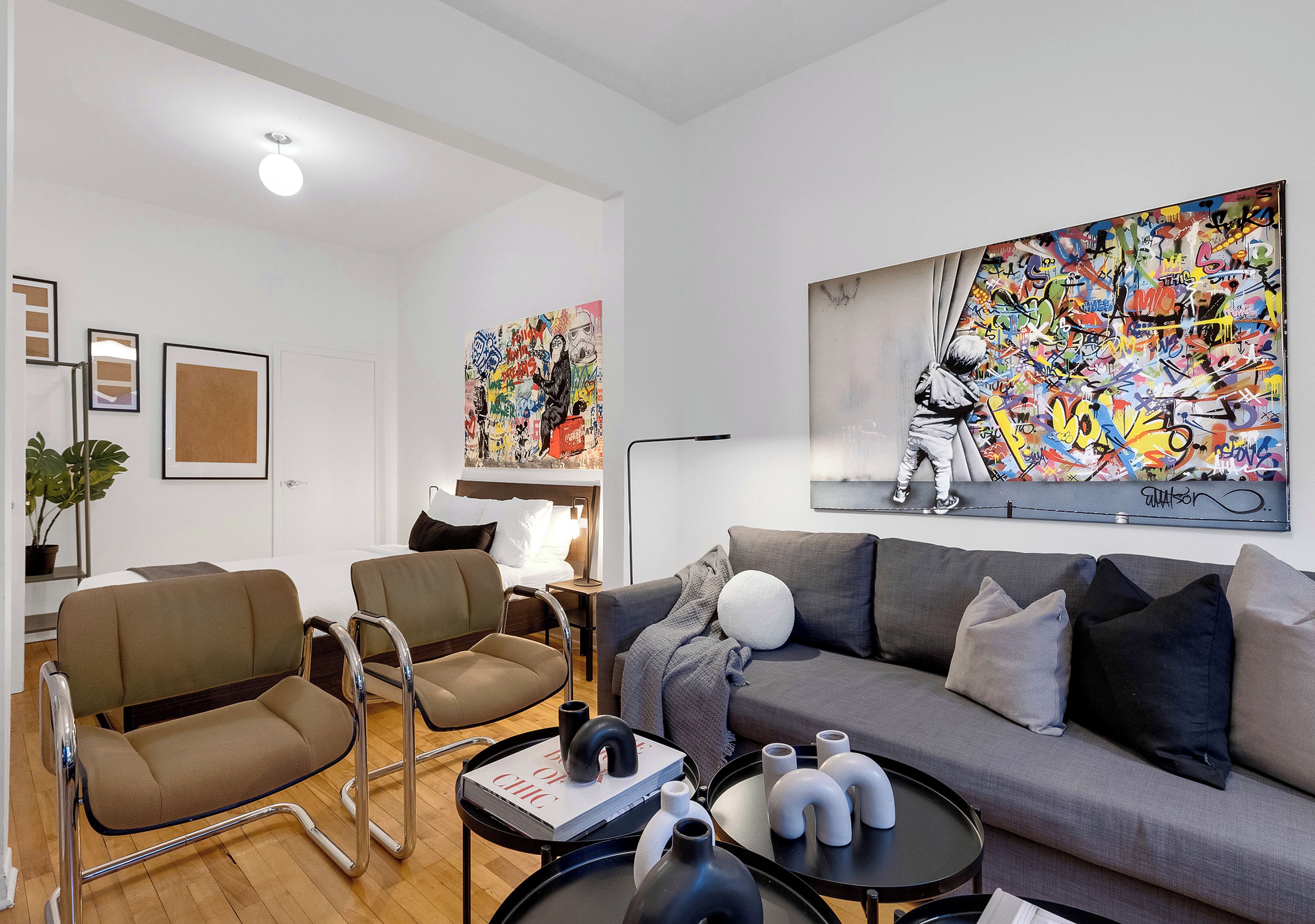 Una sala de estar moderna con un sofá gris, dos sillones, una mesa de centro con objetos decorativos y dos grandes cuadros abstractos en la pared.