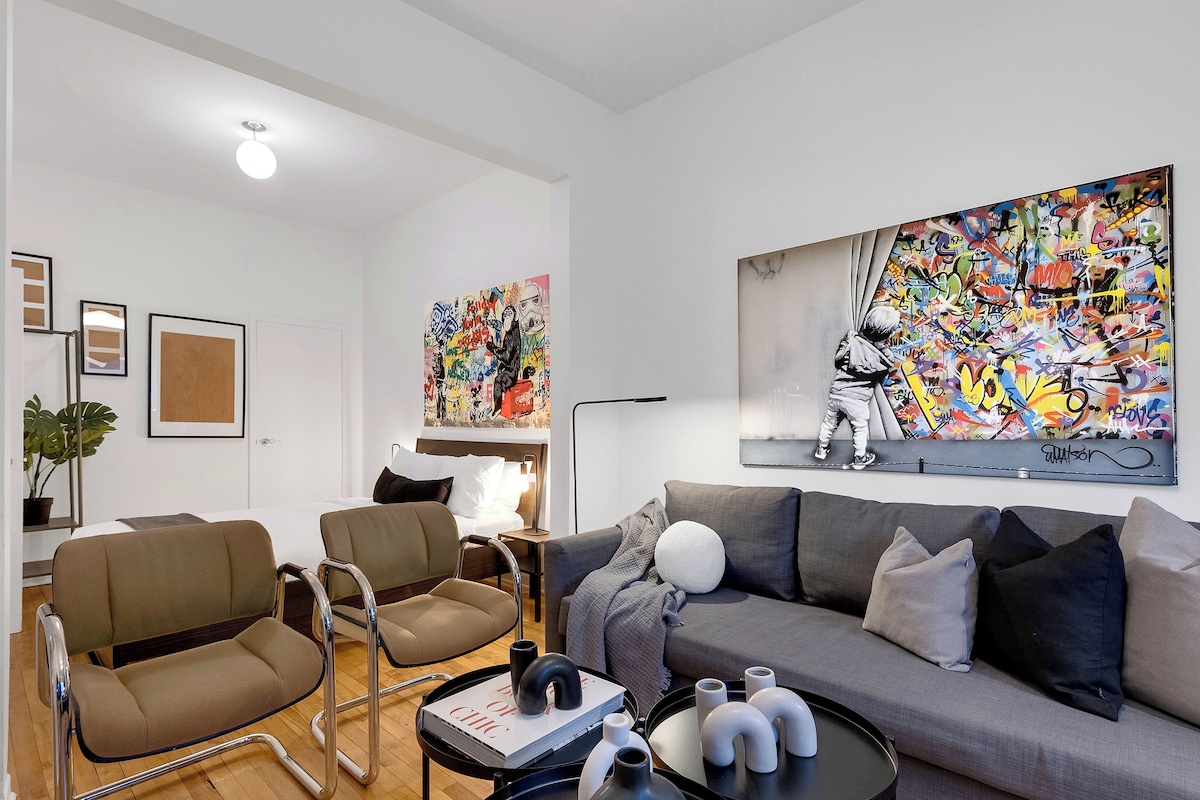 A modern living room with a grey sofa, two armchairs, a coffee table with decorative items, and two large abstract paintings on the wall.