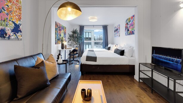 A modern hotel room with a bed, sofa, TV, and artwork. -  LiV MTL - Avenue (Montreal)