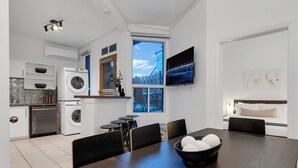 A modern kitchen with a washing machine, dining area with a table and chairs, and a TV mounted on the wall. -  LiV MTL - Avenue (Montreal)