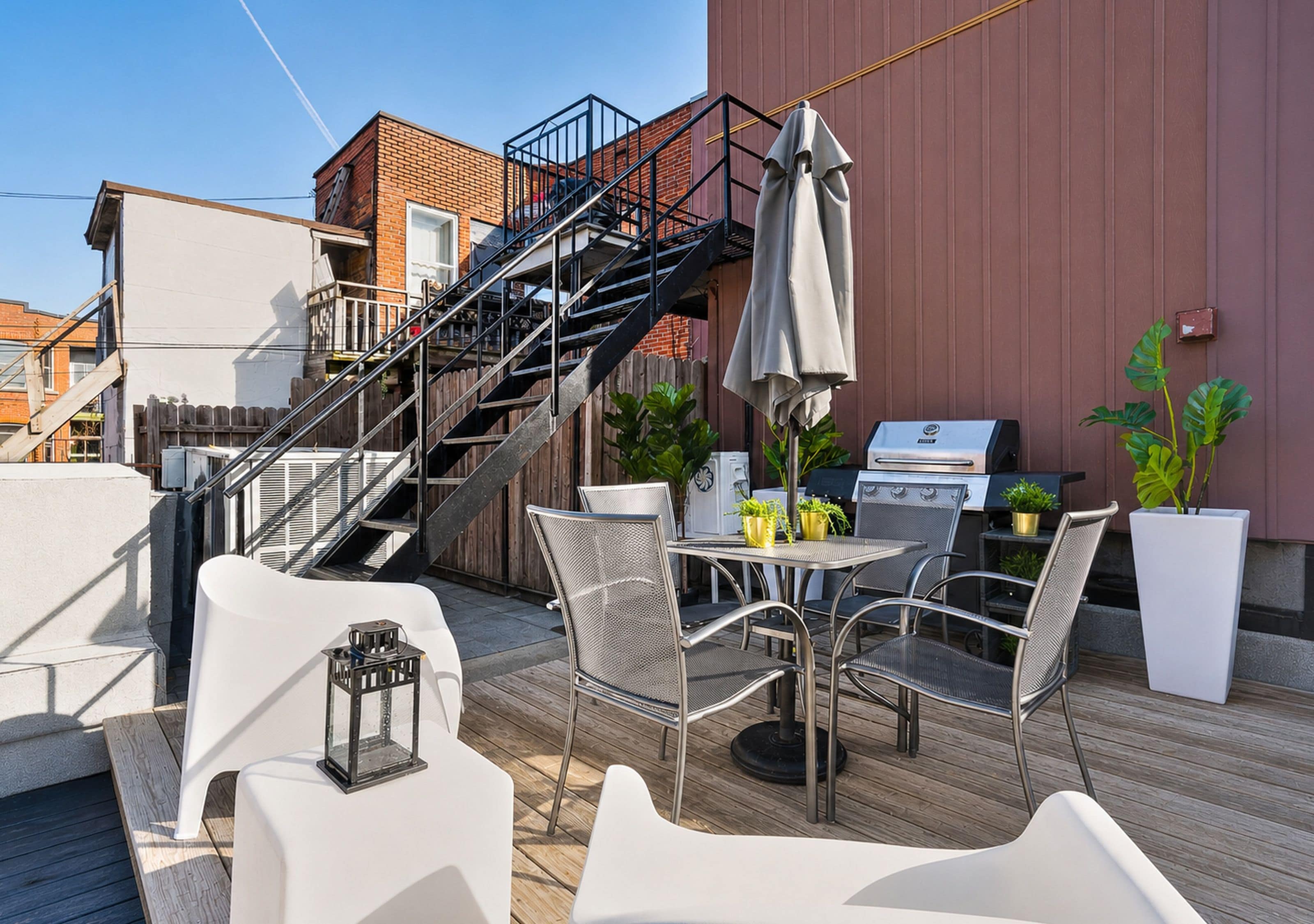 Eine Dachterrasse mit Gartenmöbeln, einem Grill und einer Treppe zu einer oberen Ebene.