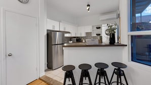 A modern kitchen with a stainless steel refrigerator, white cabinets, a microwave, and a small island with stools. -  LiV MTL - Avenue (Montreal)