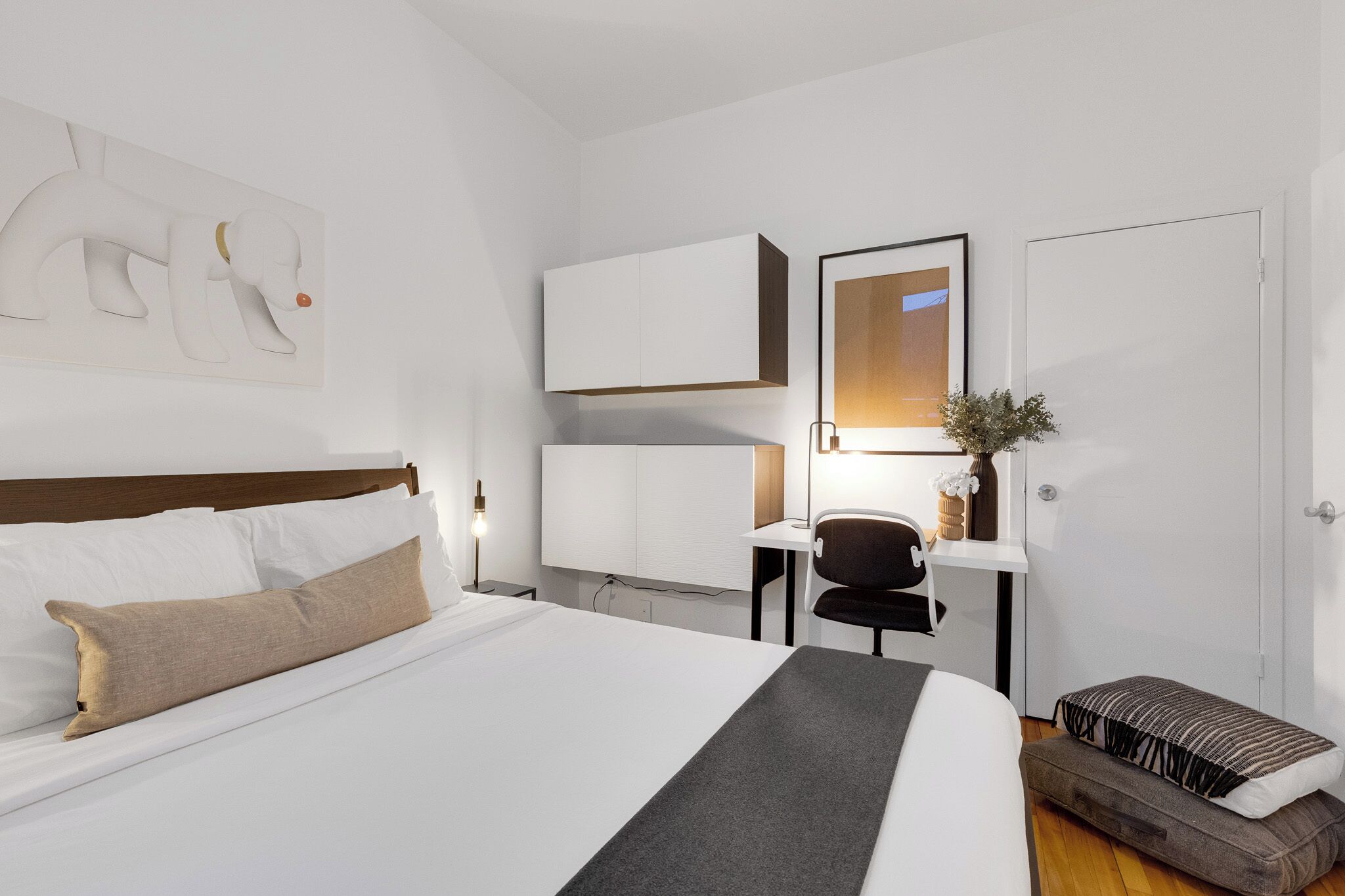 A hotel room with a bed, a desk, a chair, a mirror, and a door.