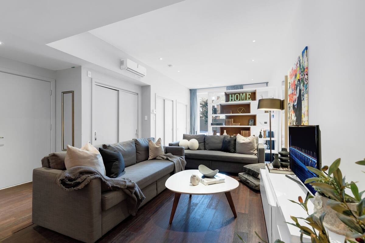 A modern living room with a grey sofa, a white coffee table, and a bookshelf in the background.