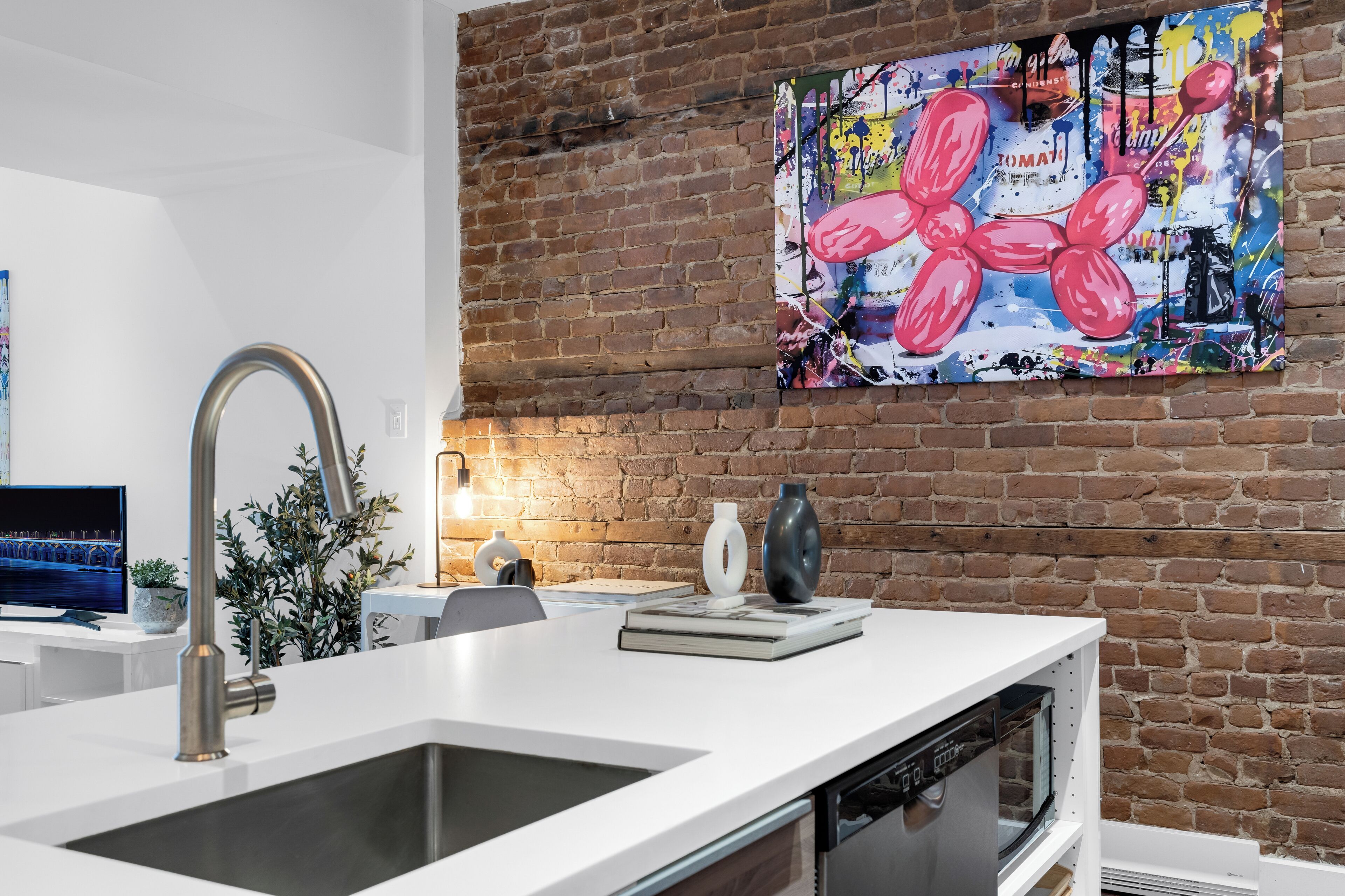 Une cuisine dotée d’un robinet moderne, d’un mur en briques et d’un tableau abstrait aux couleurs vives.