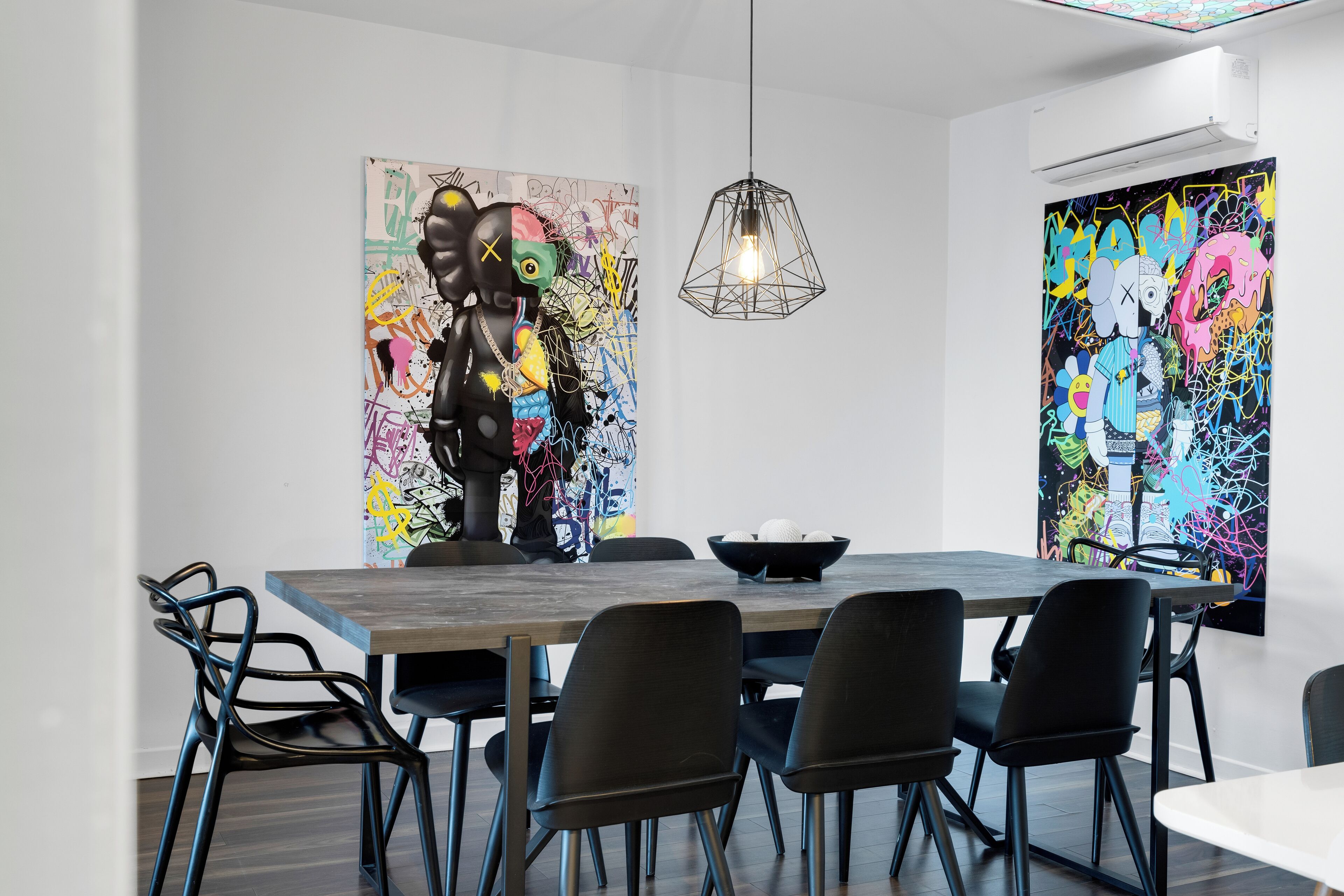 A modern dining area with a wooden table, black chairs, and two abstract paintings on the walls.