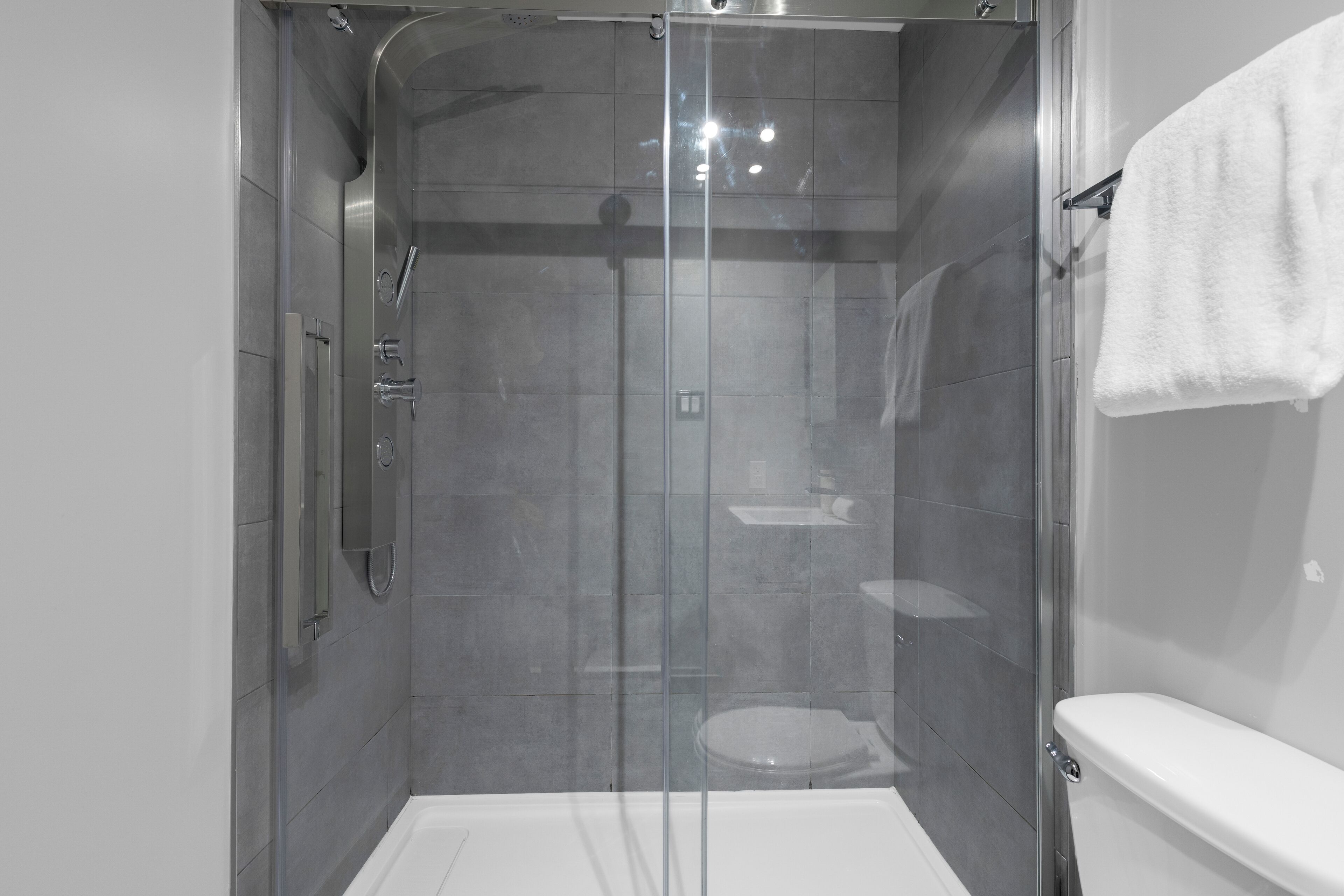 A modern bathroom with a glass-enclosed shower, a white toilet, and a towel hanging on the wall.