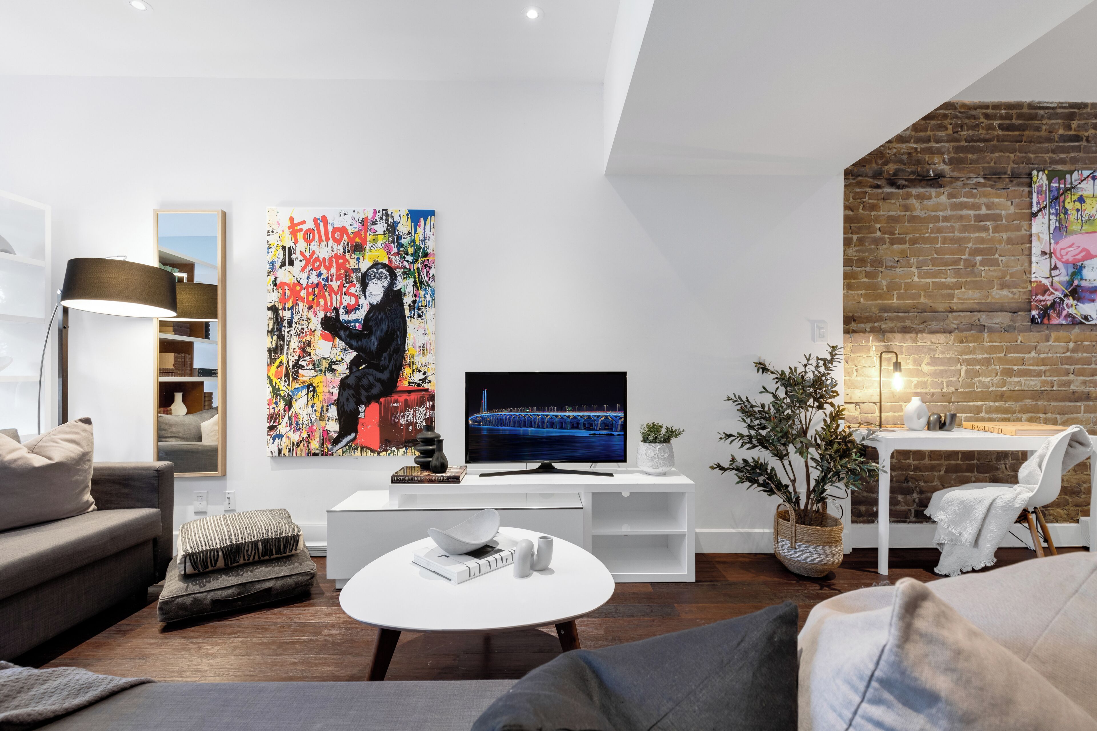 A modern living room with a flat-screen TV, a large abstract painting, and a brick wall.
