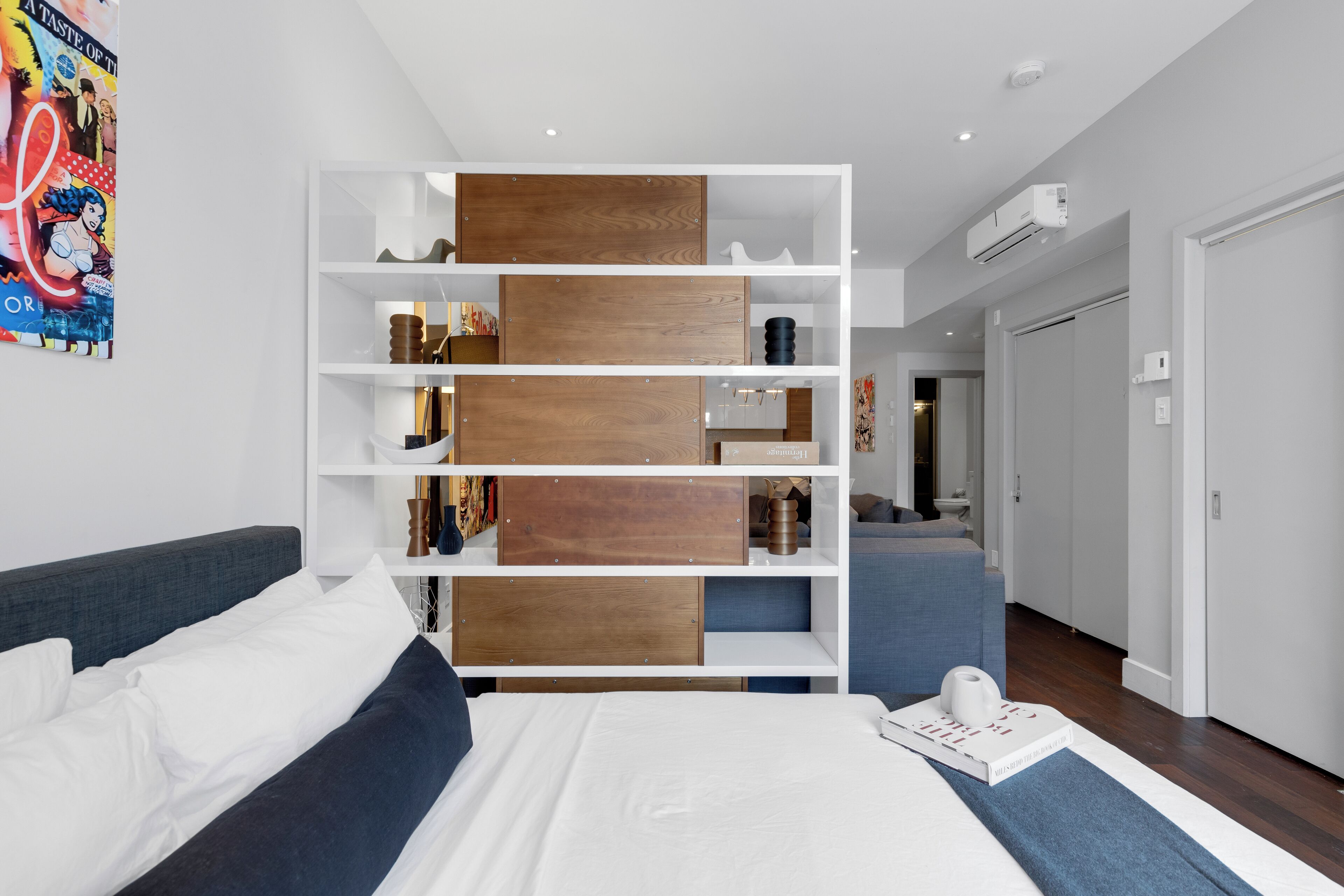 A modern bedroom with a bed, a white wardrobe with wooden panels, and a poster on the wall.